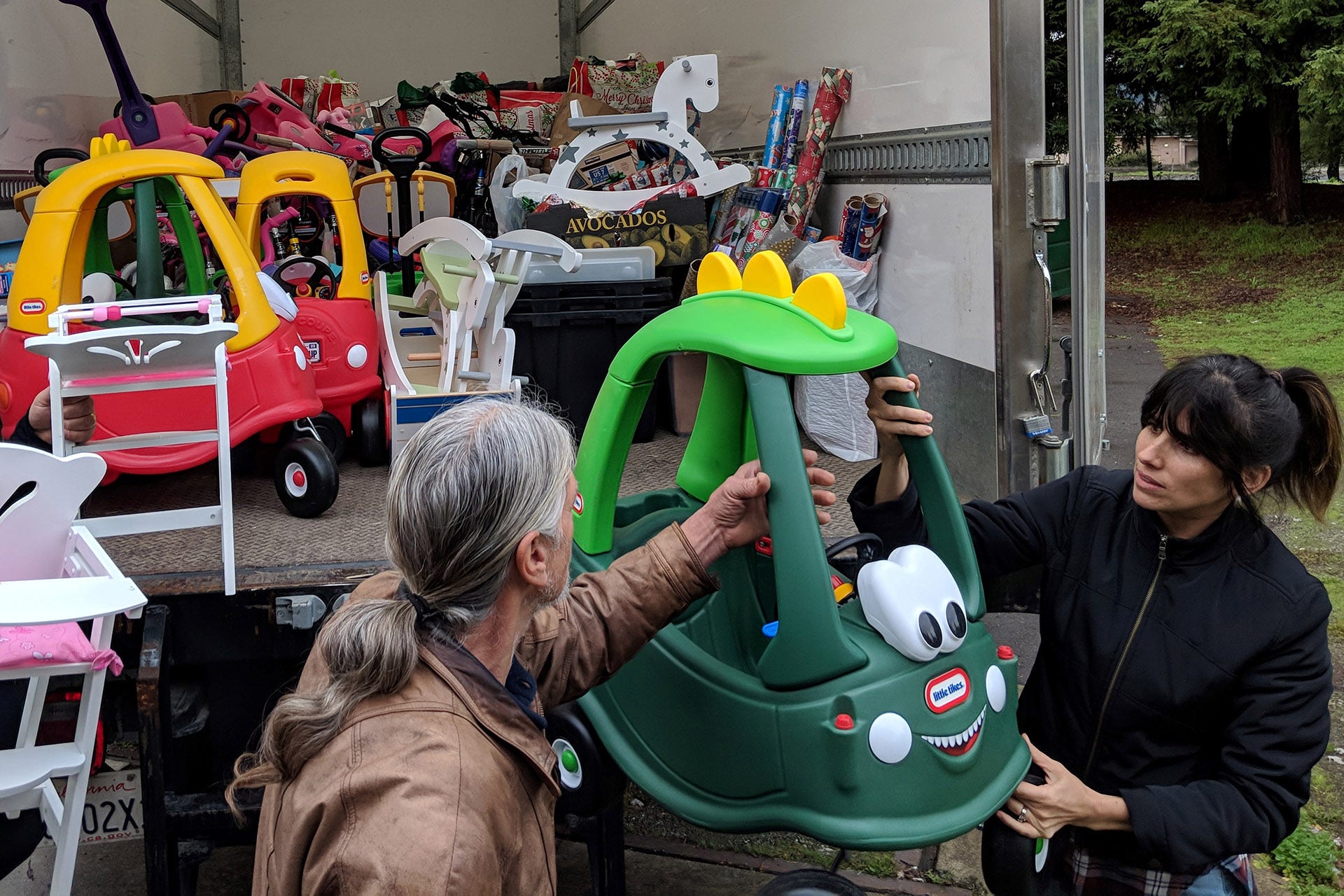 A man and a woman unloading a truck filled wtih toys for young children
