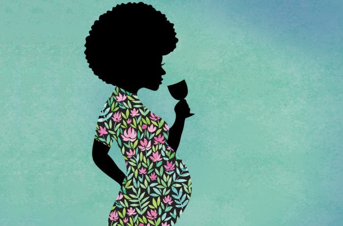 A woman drinking a glass of wine while pregnant.