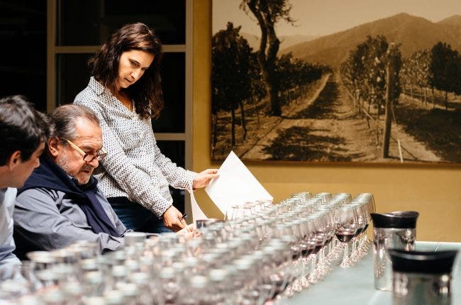 Winemaker Rebecca Wineburg talks with Michel Roland in front of rows of sample wine glasses