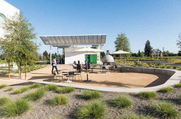 A photograph of an outdoor tasting space and modern building on the grounds of Ashes & Diamonds Winery in Napa, California.