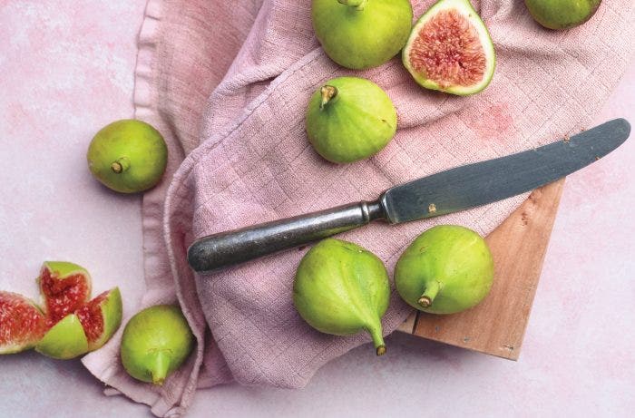 Overhead shot of fresh green figs on a pink background.