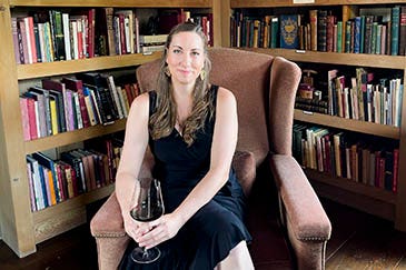 Mary Margaret McCamic in high-backed chair surrounded by books, holding glass of red wine