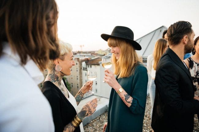 Two tattooed young women drinking white wine at a rooftop party