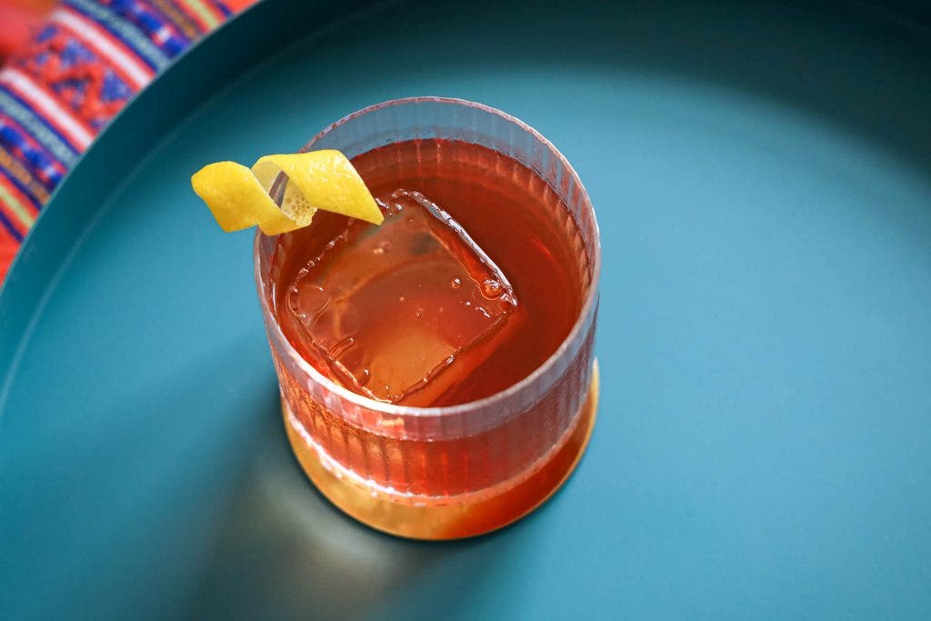 Vieux Carré cocktail on blue tray with large ice cube and lemon twist